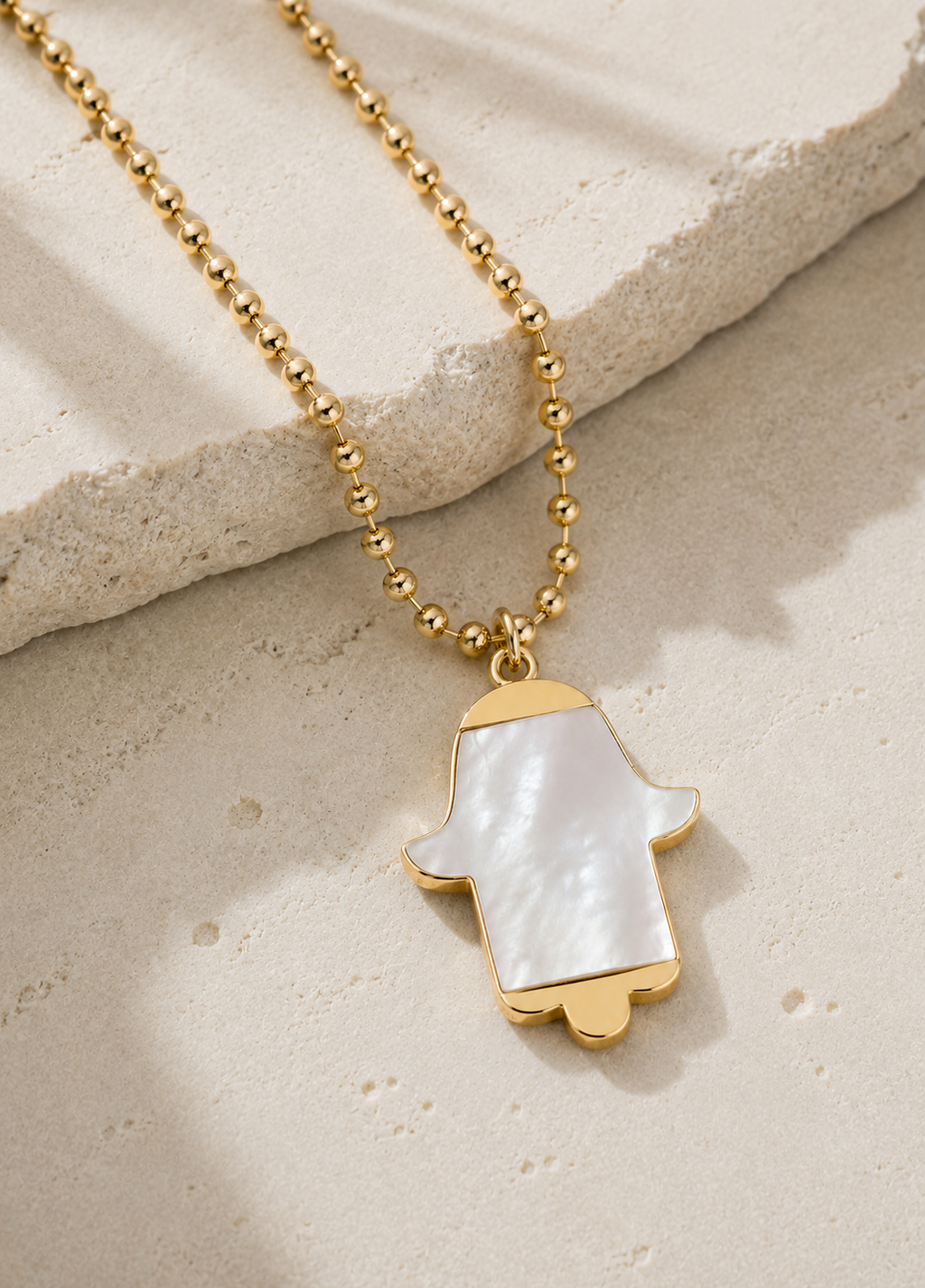 MOP Hamsa Necklace displayed on a luxury neutral stone surface.
