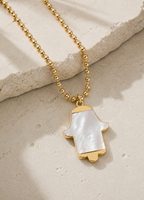 MOP Hamsa Necklace displayed on a luxury neutral stone surface.