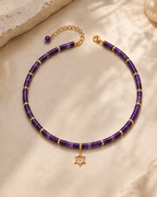 Noa Star of David Beaded Choker Necklace in Amethyst with gold tone details on neutral stone surface.