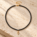 Adele Hamsa Beaded Necklace in Black with gold tone details on neutral stone surface.