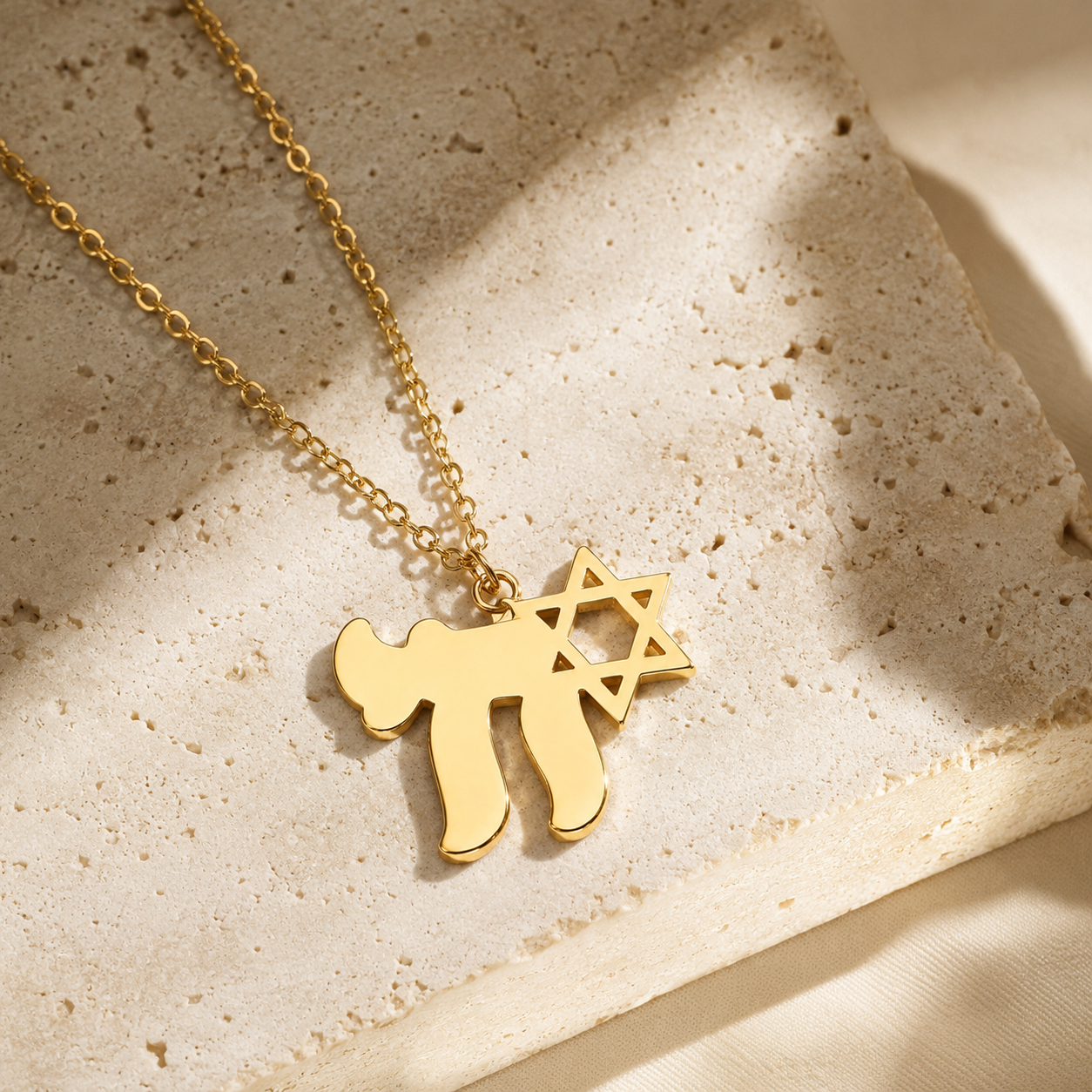 Gold tone Am Yisrael Chai necklace styled on a neutral stone surface.