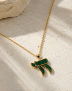 Gold tone Perlée Chai Necklace in green styled on a neutral stone surface.