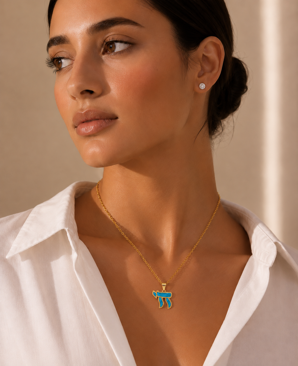 Model wearing the gold tone Perlée Chai Necklace with a turquoise Chai pendant.