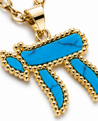 Close-up of the turquoise Chai pendant with gold tone detailing.