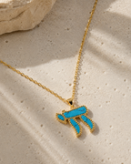 Gold tone Perlée Chai Necklace with a turquoise Chai pendant styled on a neutral stone surface.