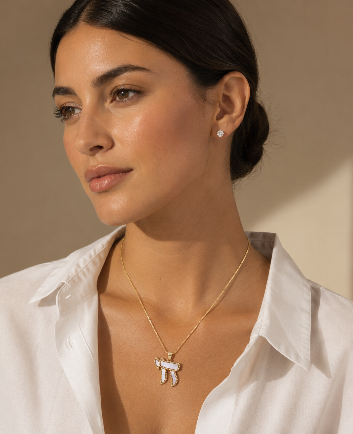 Model wearing the gold tone Perlée Chai Necklace with white pearl-effect detailing.