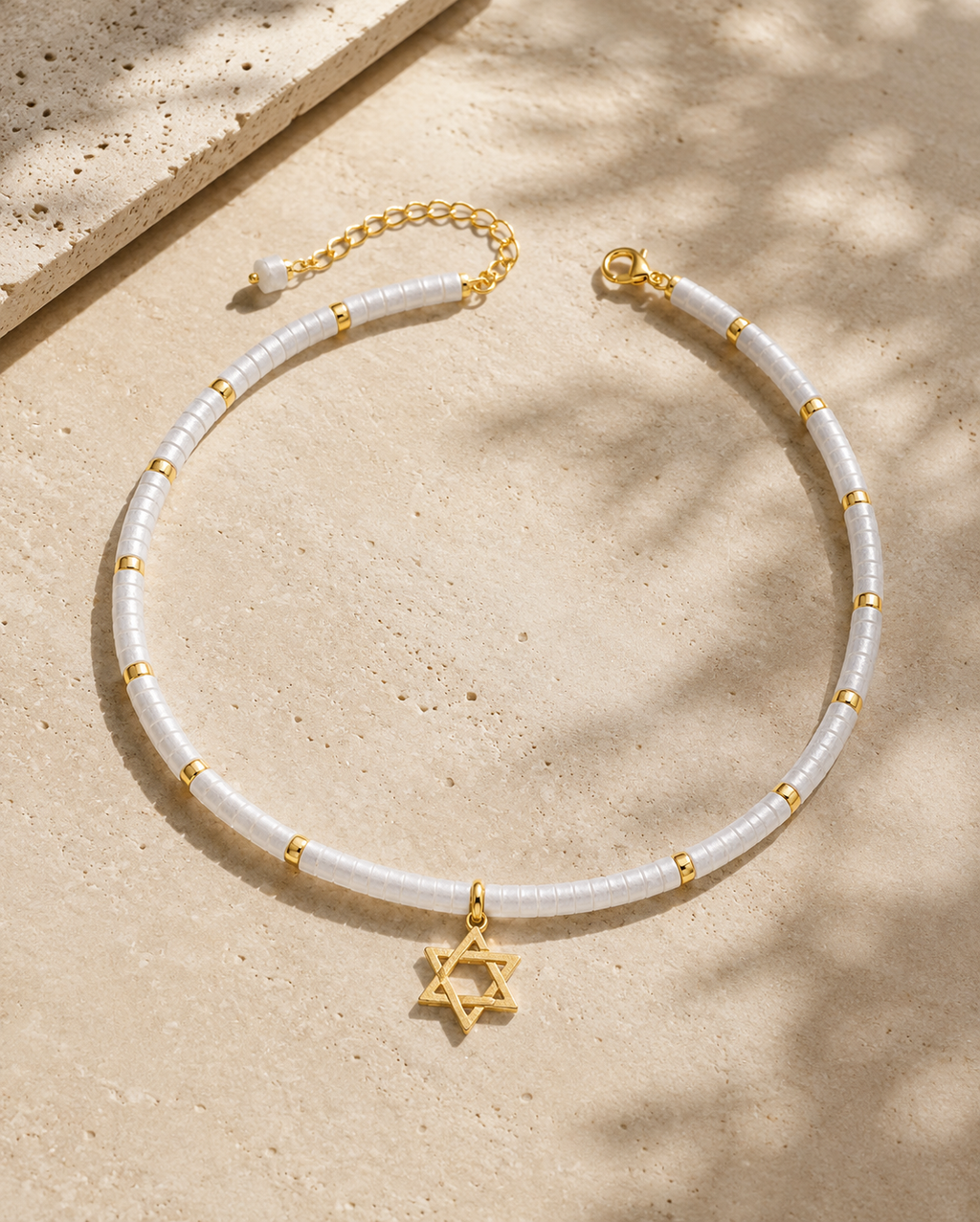 Clear quartz Magen David necklace with gold tone Star of David pendant styled on a neutral stone surface.