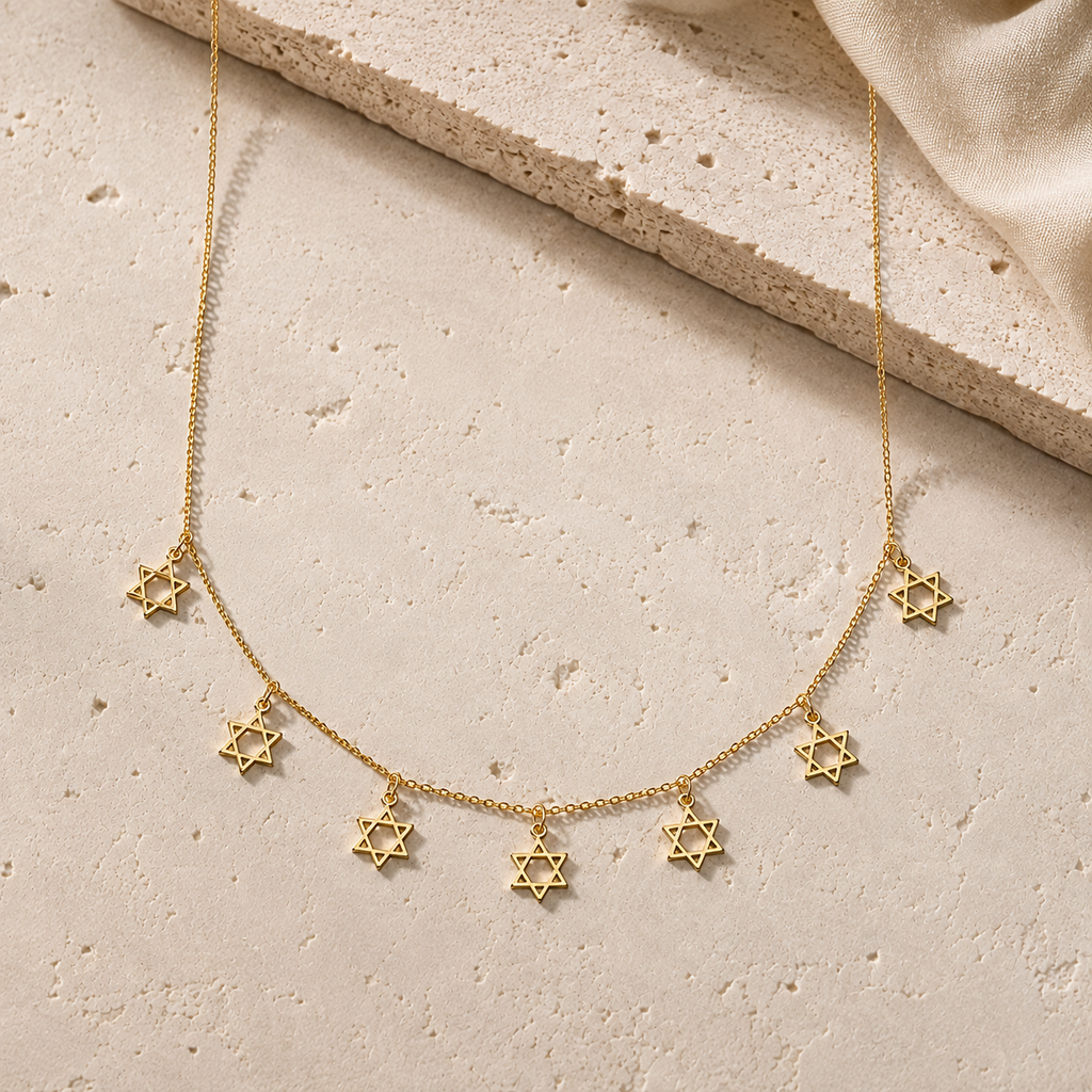 Gold Tone Divine Protection Necklace with seven Star of David charms displayed on a luxury neutral stone surface.