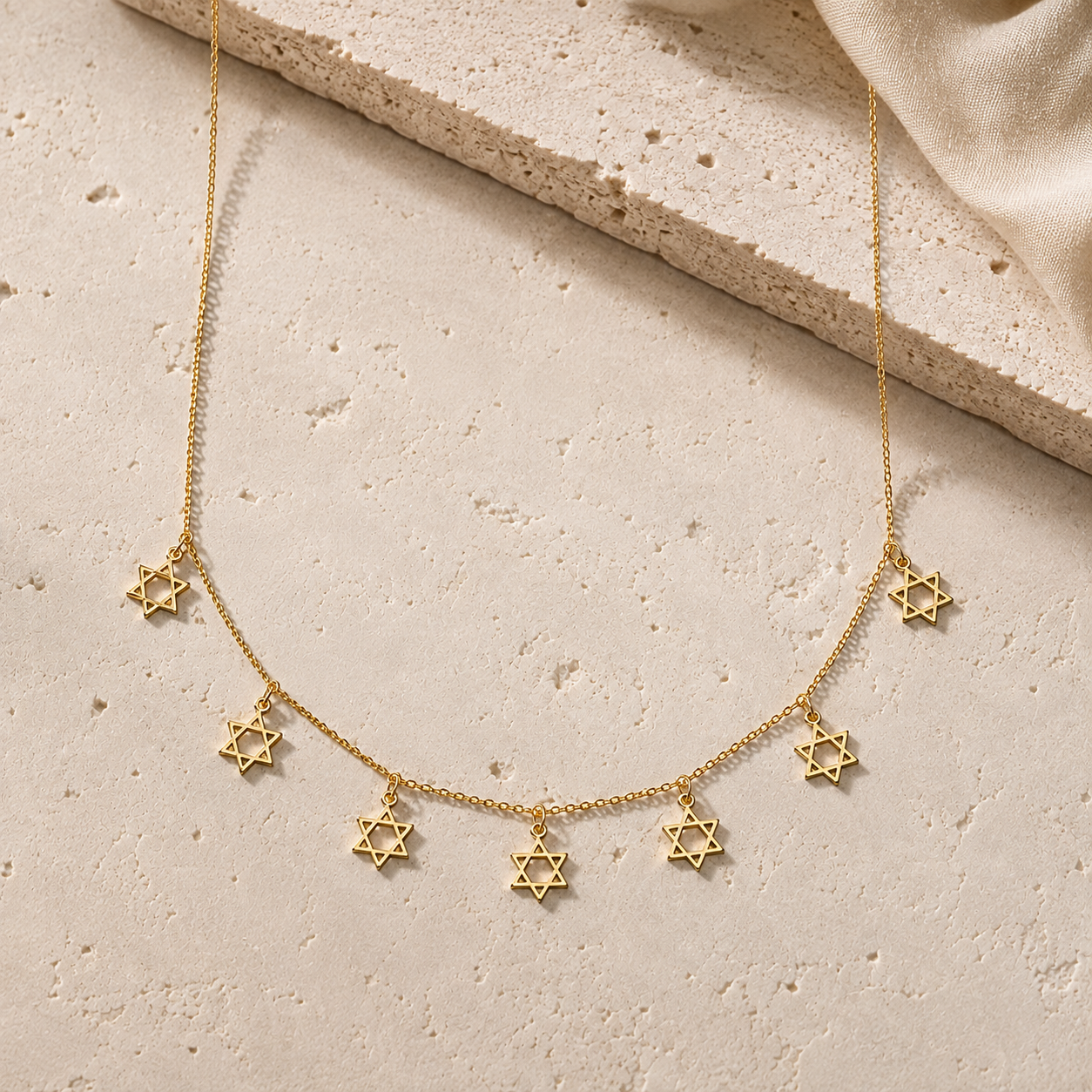 Gold Tone Divine Protection Necklace with seven Star of David charms displayed on a luxury neutral stone surface.