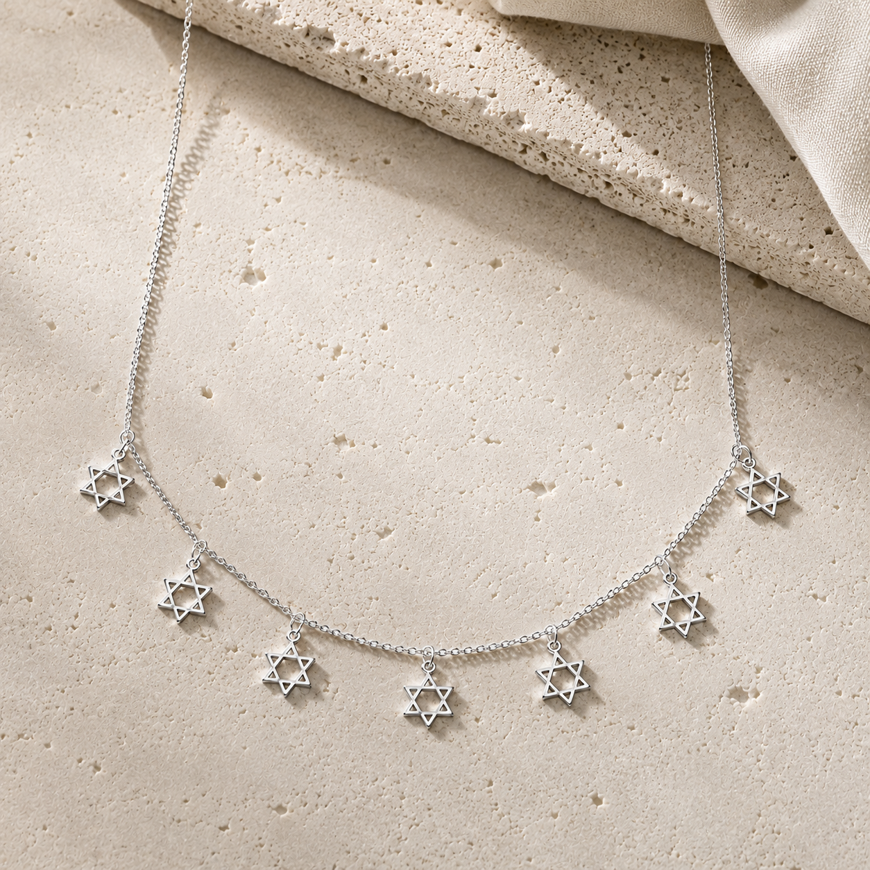 Silver Tone Divine Protection Necklace with seven Star of David charms displayed on a luxury neutral stone surface.