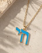 Gold tone Enamel Chai Necklace with blue enamel detailing styled on a neutral stone surface.