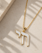 White enamel Chai necklace styled on a neutral stone surface.