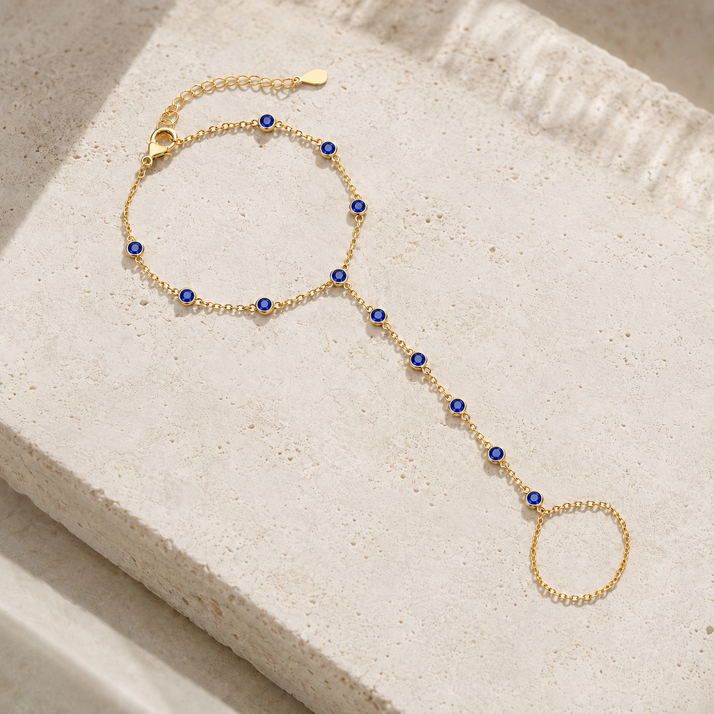 Gold tone Hava CZ Hand Chain with sapphire-colored cubic zirconia styled on natural stone.