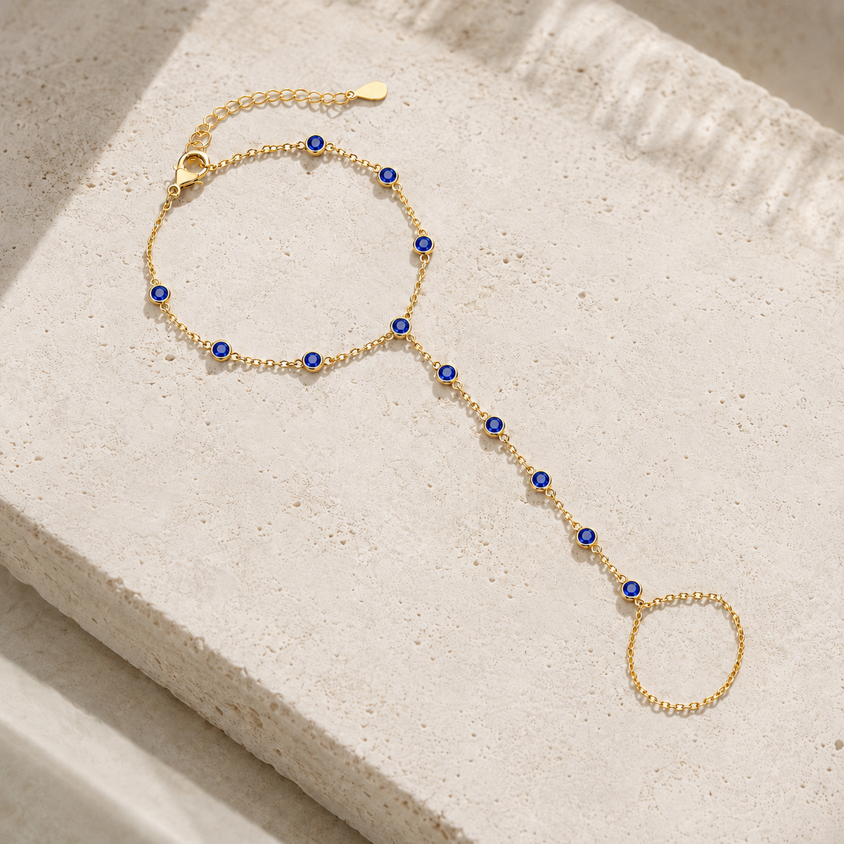 Gold tone Hava CZ Hand Chain with sapphire-colored cubic zirconia styled on natural stone.