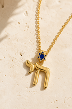 Gold tone Jerusalem Chai Necklace with navy enamel Star of David detailing styled on a neutral stone surface.
