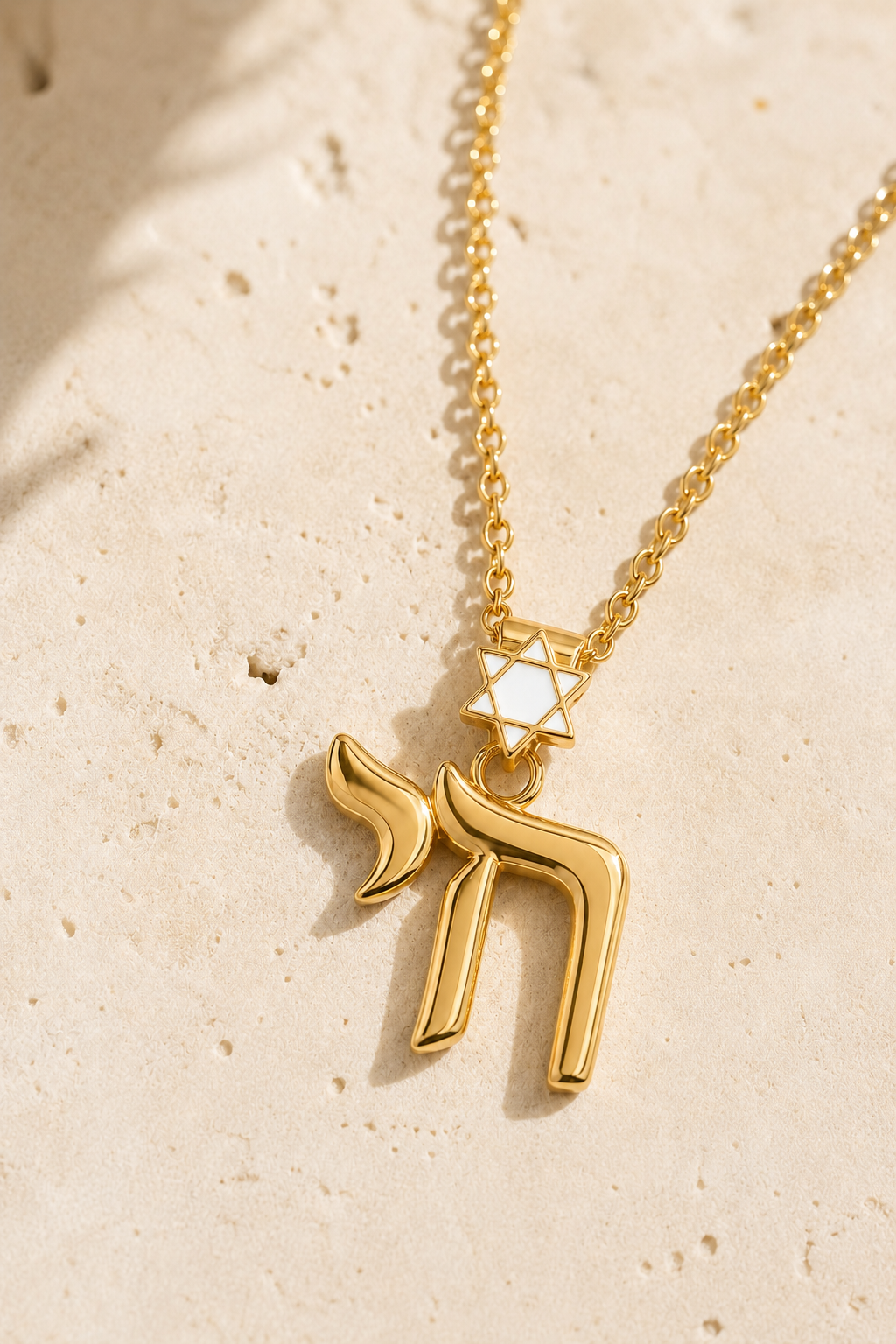 Gold tone Jerusalem Chai Necklace with white enamel Star of David detail styled on a neutral stone surface.