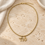 Neshama Charm Necklace arranged on pale travertine beside ivory linen and an ivory ceramic dish.