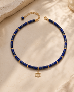 Noa Star of David Beaded Choker Necklace in Lapis with gold tone details on neutral stone surface.