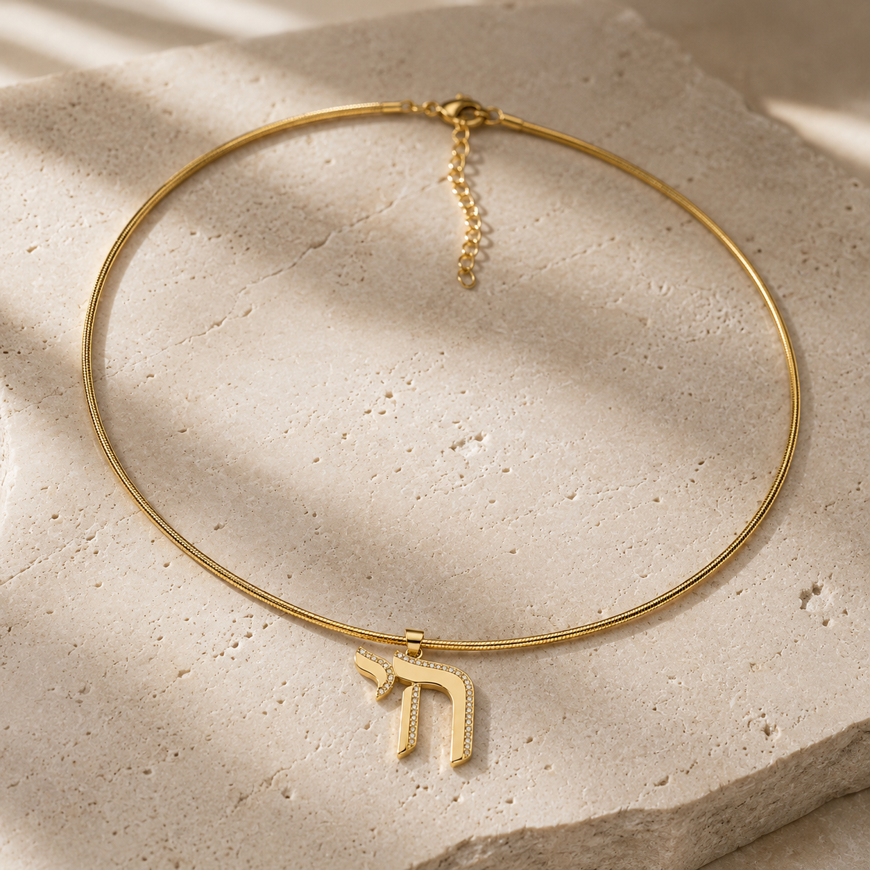Gold tone Outline Pavé Chai choker styled on a neutral stone surface.