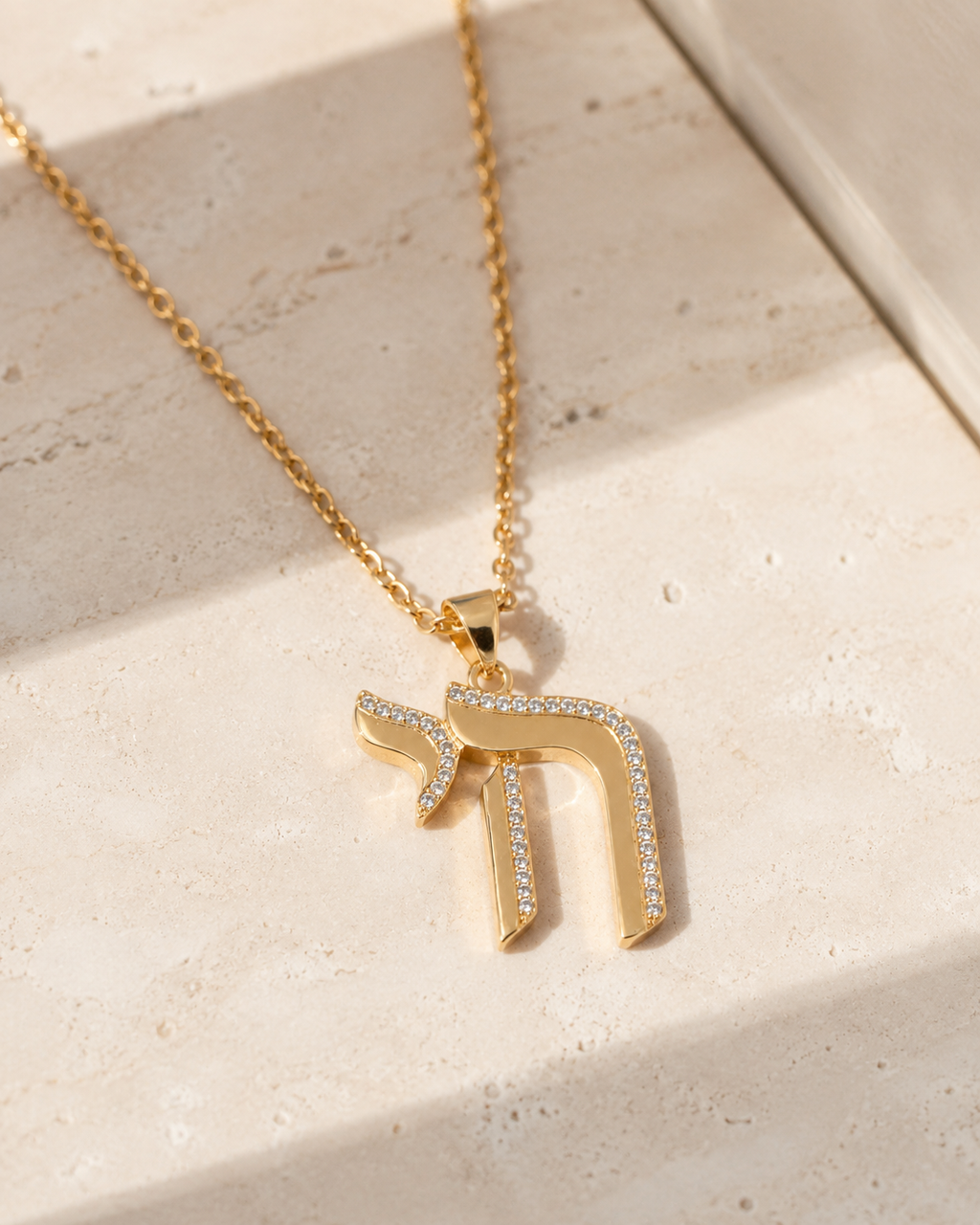 Gold tone Outline Pavé Chai Necklace styled on a neutral stone surface.