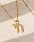 Gold tone Outline Pavé Chai Necklace styled on a neutral stone surface.