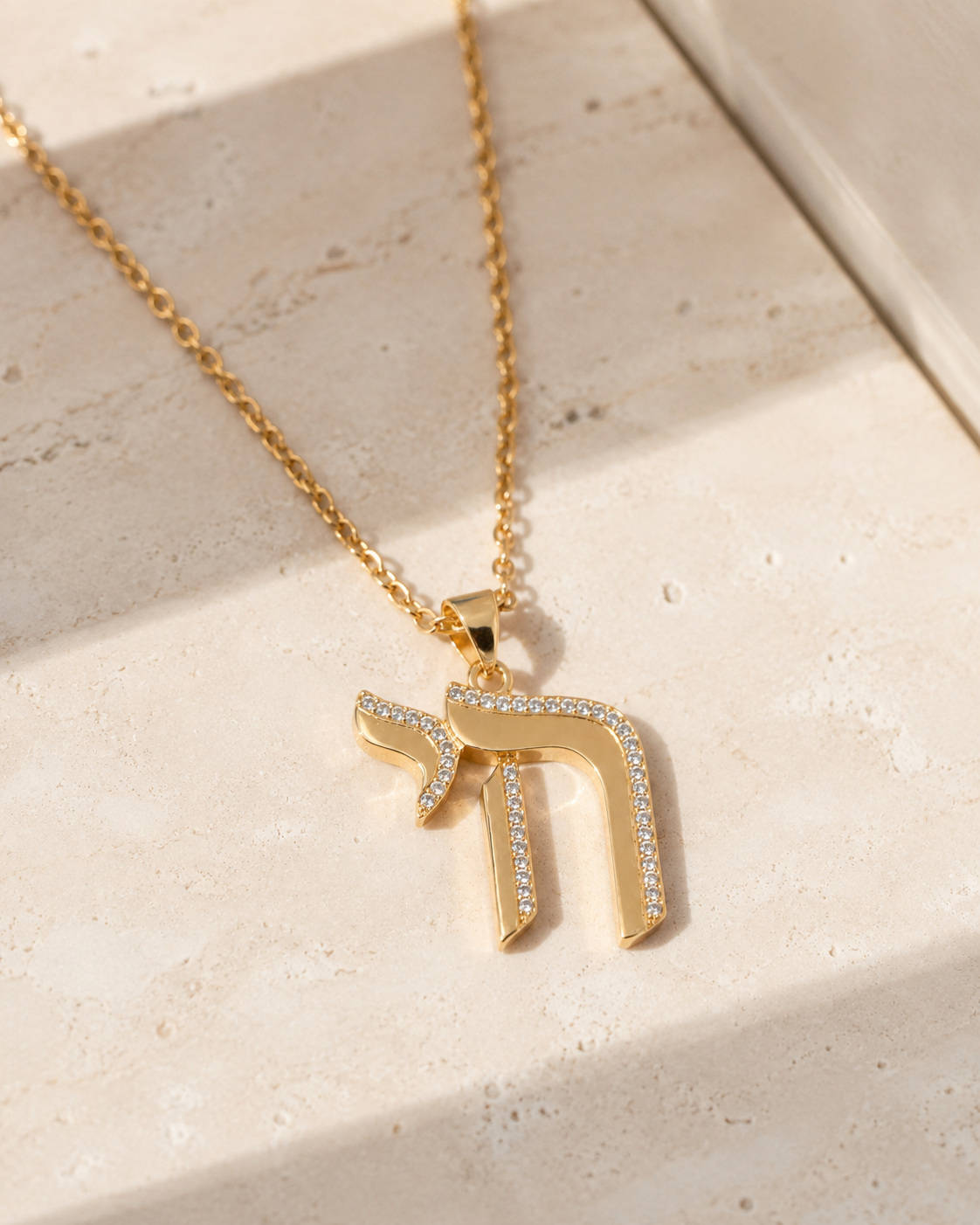 Gold tone Outline Pavé Chai Necklace styled on a neutral stone surface.