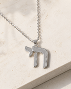 Silver tone Outline Pavé Chai Necklace styled on a neutral stone surface.