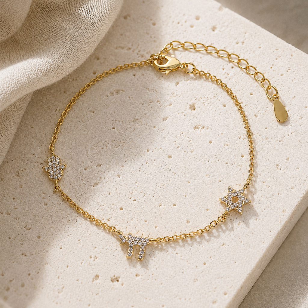 Gold Tone Pavé Trio Bracelet with Star of David, Hamsa, and Chai charms on a luxury neutral stone surface.