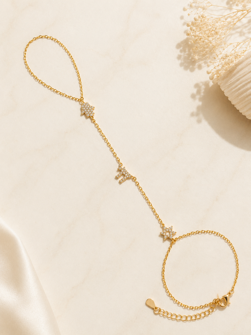 Gold tone Pavé Trio Hand Chain styled on a neutral stone surface.