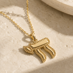 Gold tone Perlée Chai Necklace styled on a neutral stone surface.