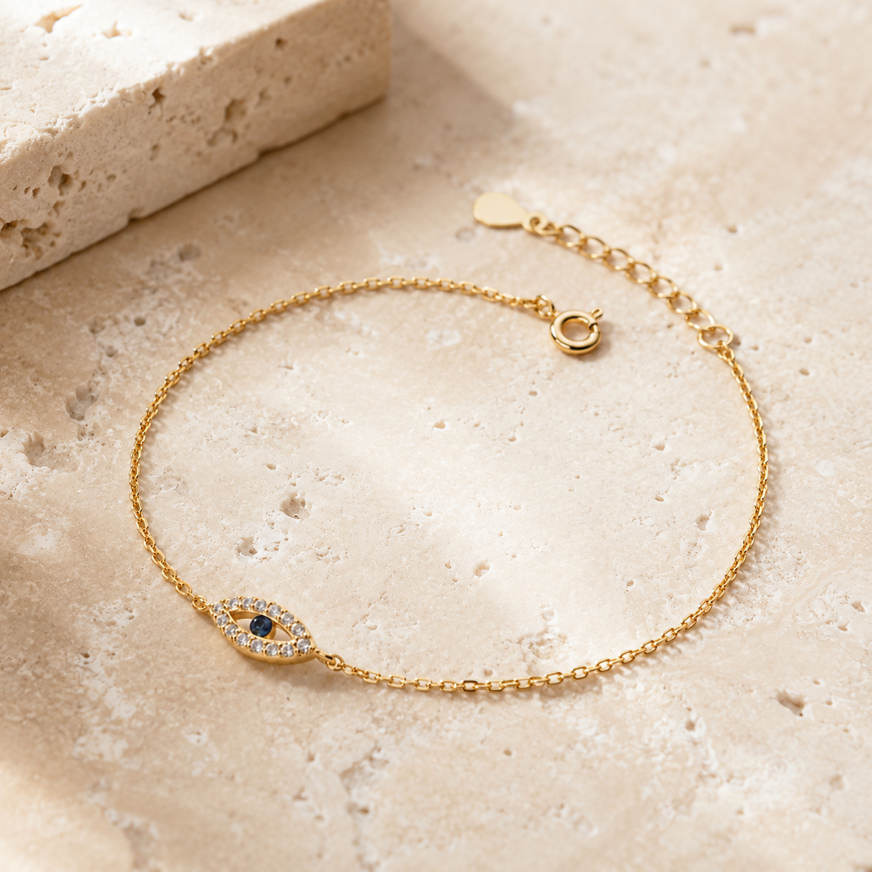 Gold tone Petite Evil Eye Bracelet styled on a neutral stone surface.