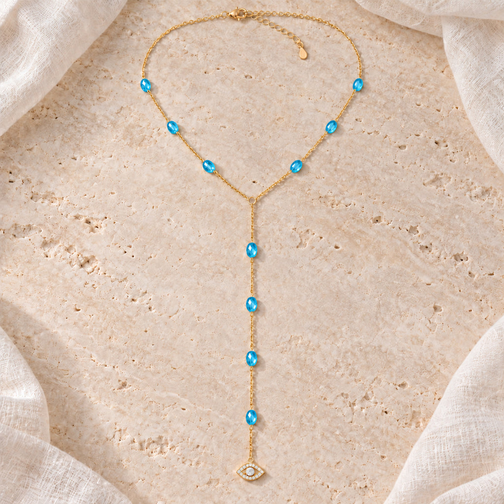 Blue See No Evil Lariat Necklace arranged on pale travertine beside ivory linen.