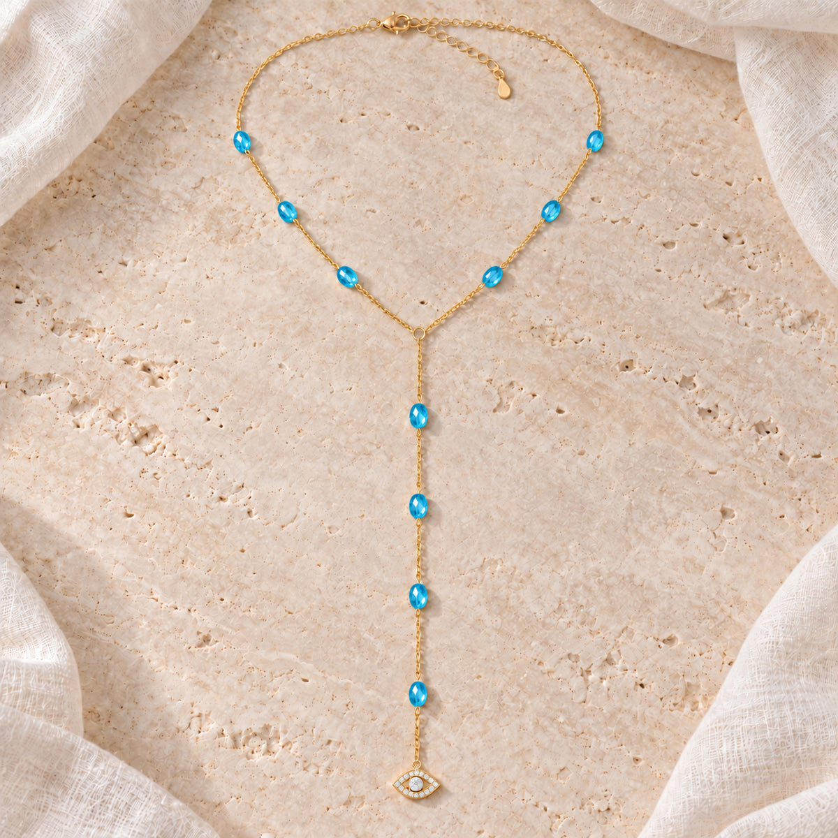 Blue See No Evil Lariat Necklace arranged on pale travertine beside ivory linen.